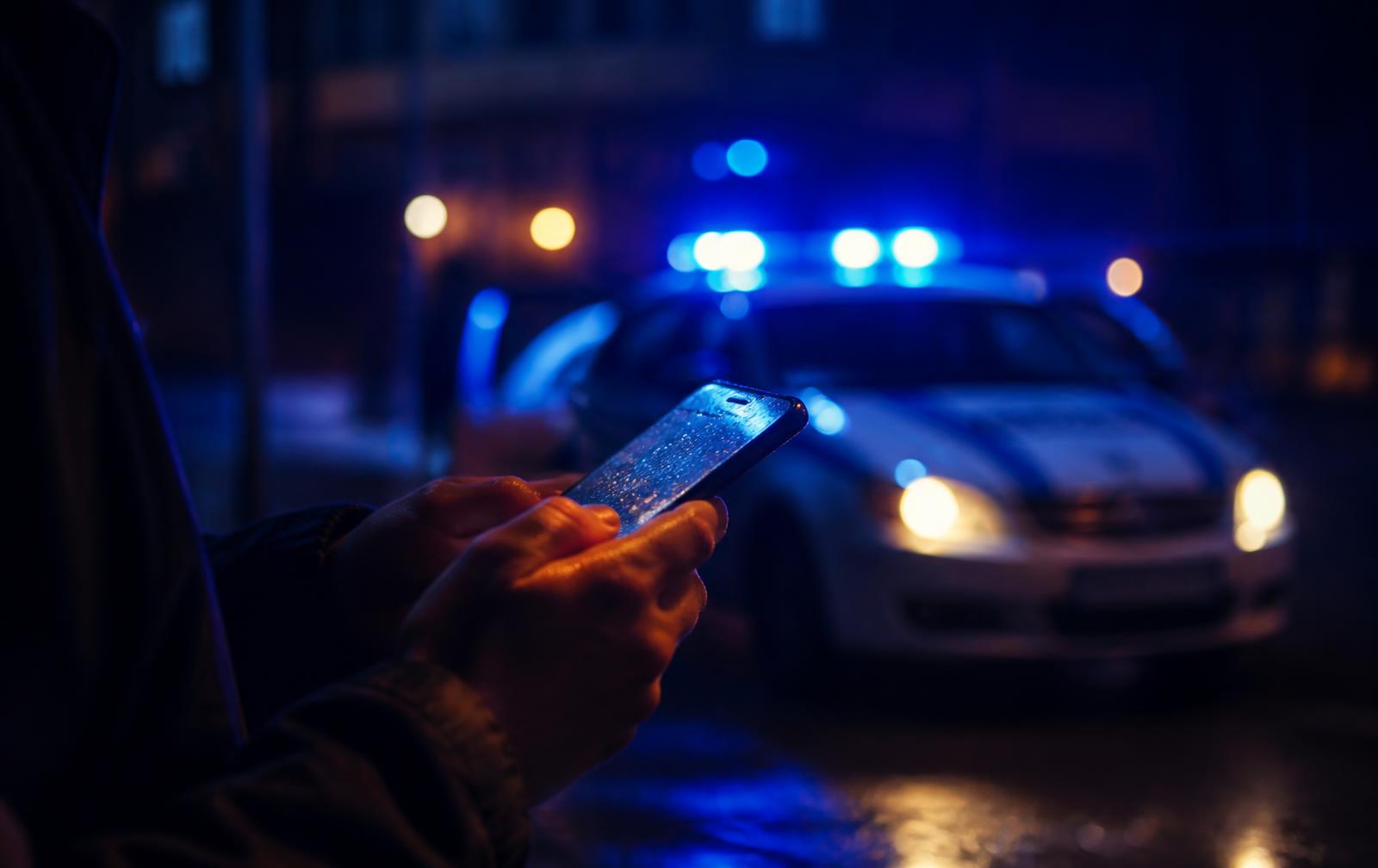 Familiar ligando para advogado criminalista à noite com viatura policial ao fundo